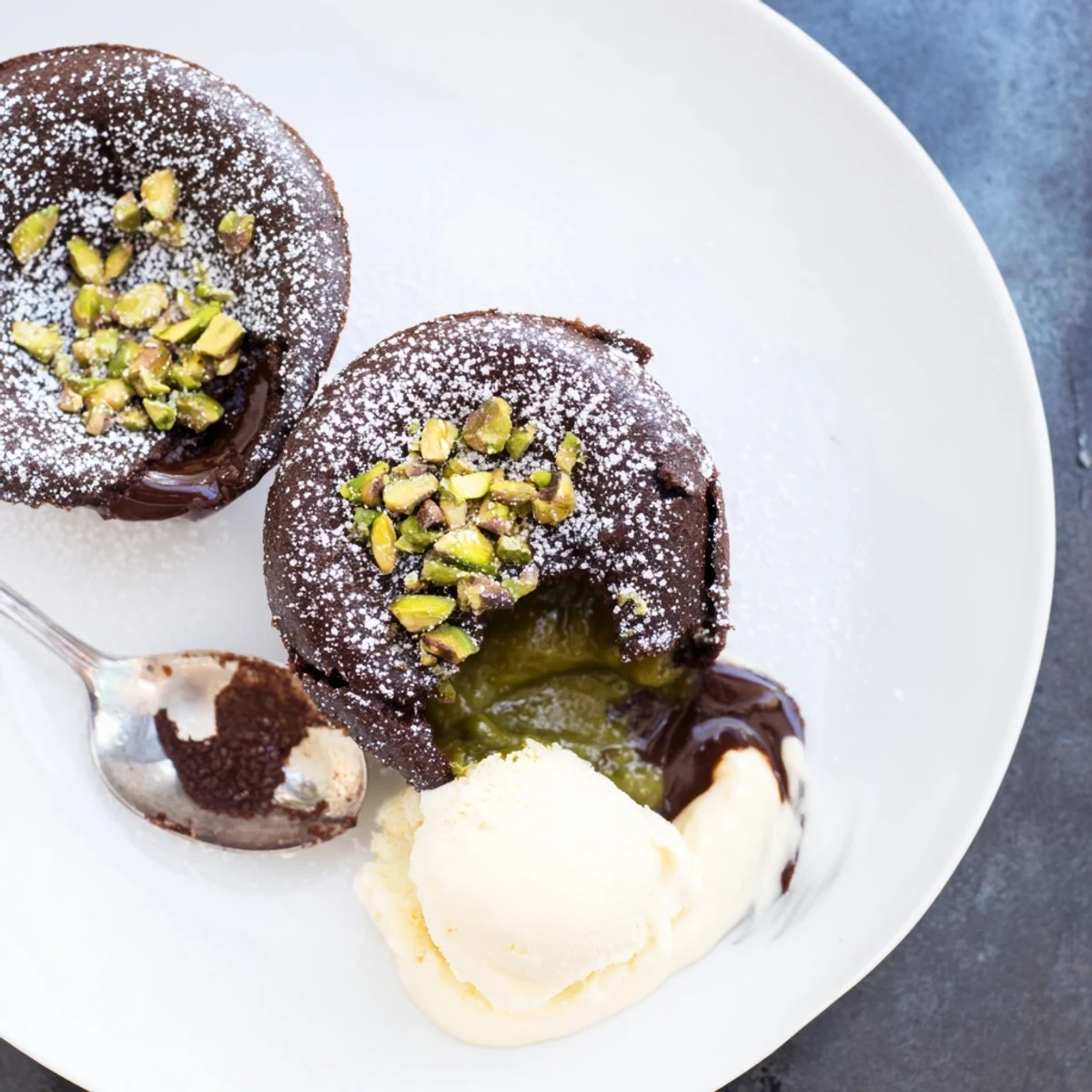 Warm pistachio chocolate lava cakes drizzled with vanilla ice cream and powdered sugar