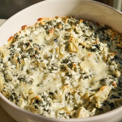 Warm Creamy Spinach and Artichoke Dip in a baking dish, topped with a golden, bubbly cheese crust.