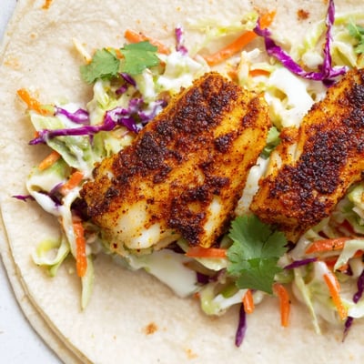 Overhead view of Cajun Spiced Fish Tacos with Slaw, featuring generously filled tortillas topped with fresh cilantro and lime wedges on the side.