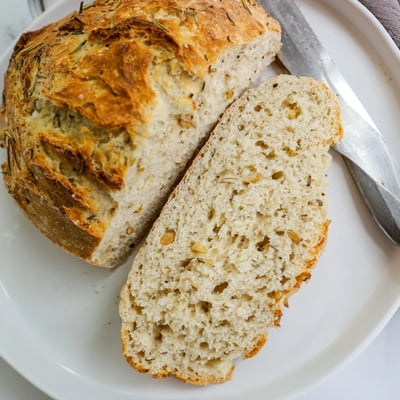 Rustic homemade Dutch oven garlic rosemary bread with fresh herbs and crisp crackling surface