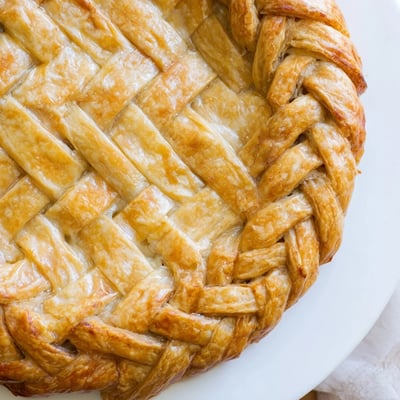 Intricate fishtail braid pie crust detailing the rim of a fruit-filled pie, showcasing buttery golden layers with a professional bakery presentation